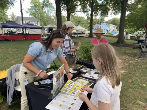 Young girl talks to woman about pollinator habitat at outdoor event
