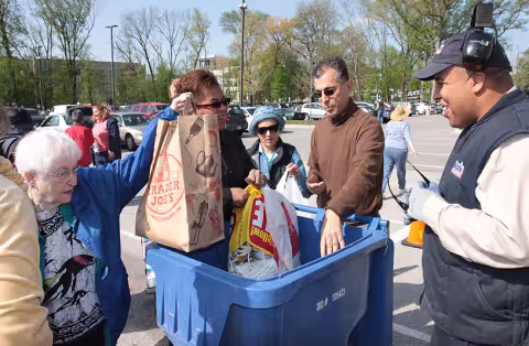 Five community members put waste into a blue bin in a parking lot